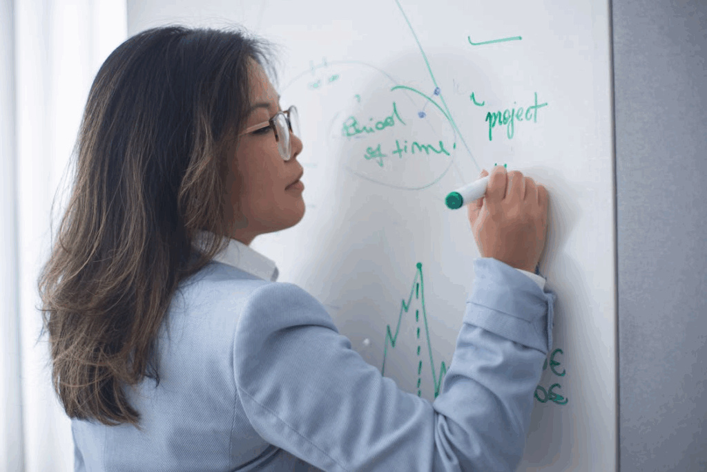 Professor explaining charts and project timelines on a whiteboard as part of a project management simulation lesson.
